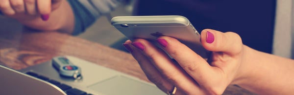 hand holding cell phone over laptop (c) William Iven 8515 unsplash